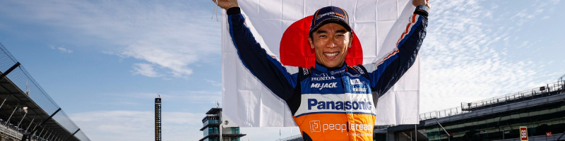 Takuma Sato standing in a victory pose at the Indy 500