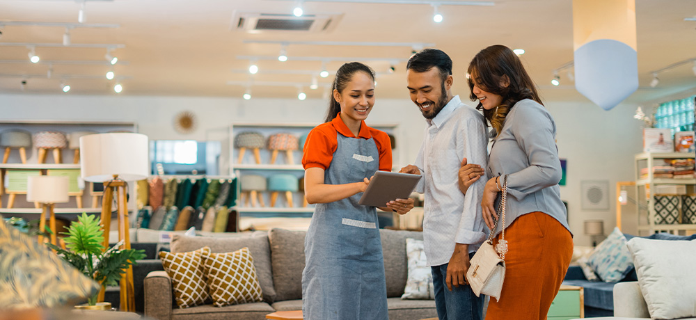Retail worker assisting customers with furniture in a retail store.