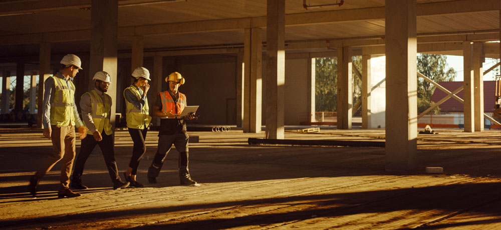 four construction workers walking a job site with hard hats and a computer