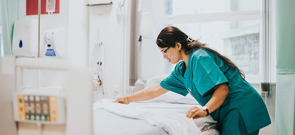 Non-clinical healthcare worker making a hospital patient bed to support patient care.